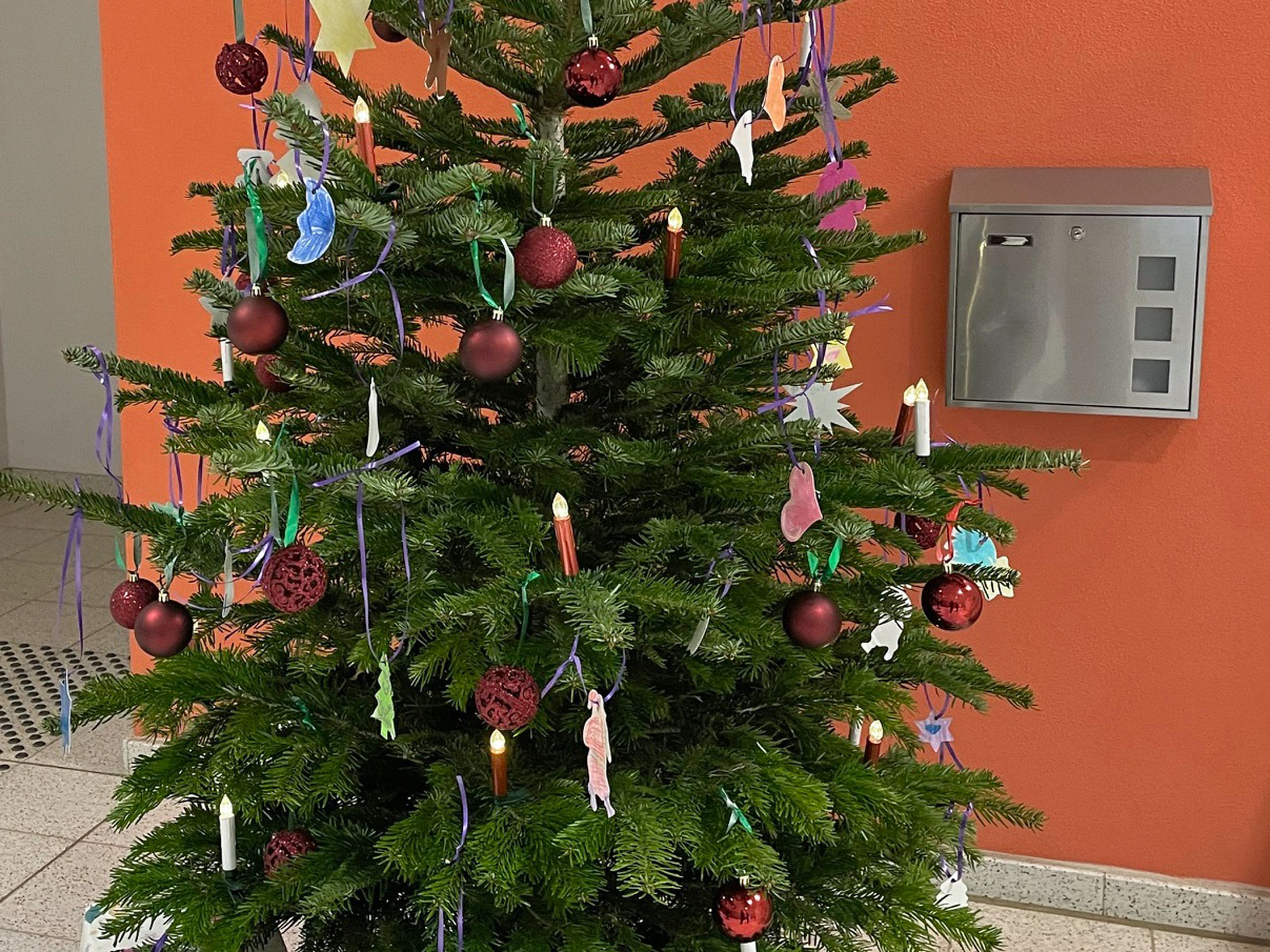 Geschmückter Weihnachtsbaum vor orangefarbener Wand.